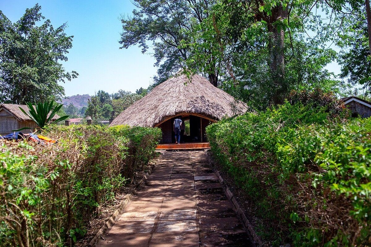 A paved path between clipped hedges leading to the thatched tomb house at Mparo Royal Tombs near Hoima