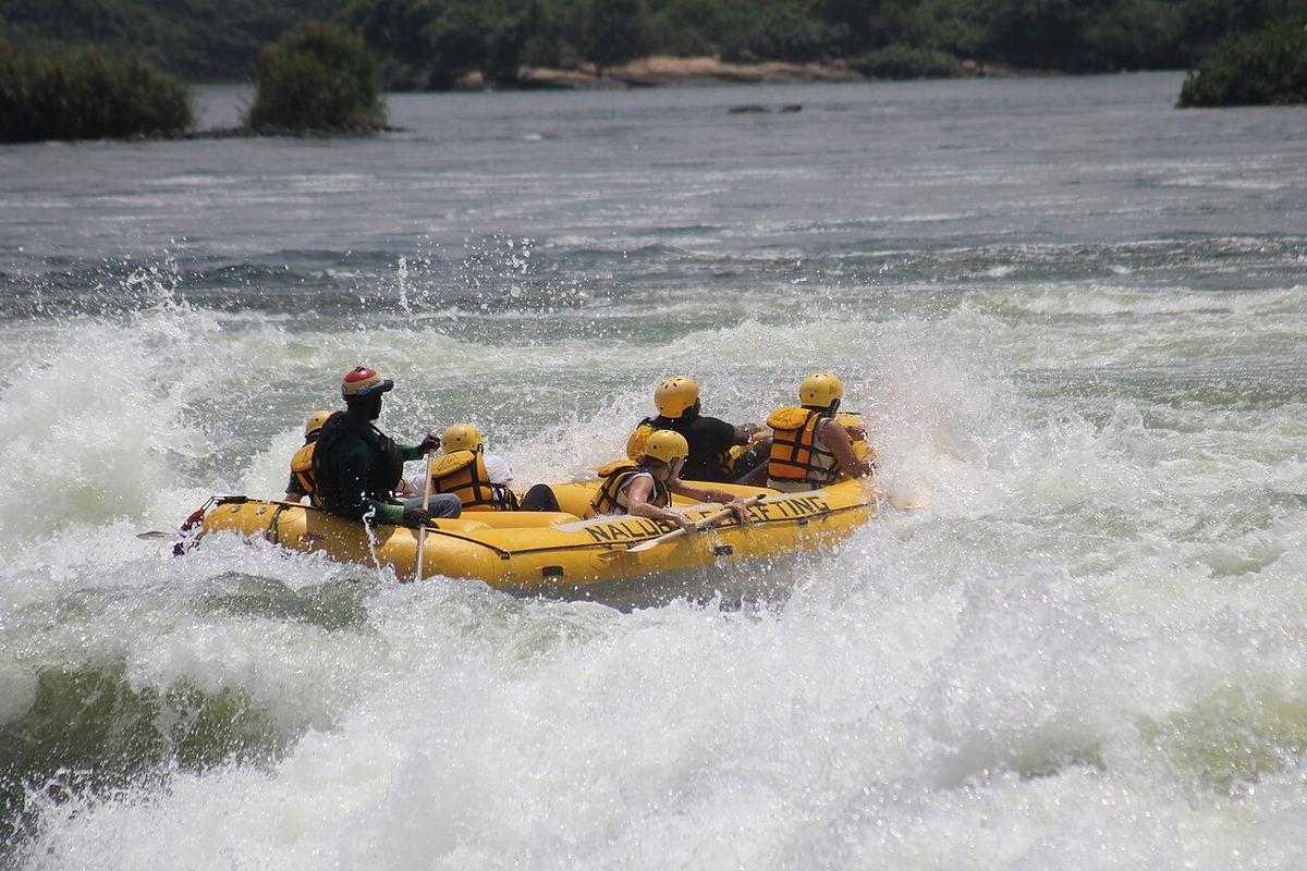 A yellow raft with helmeted paddlers punching through a white-water rapid on the Nile near Jinja