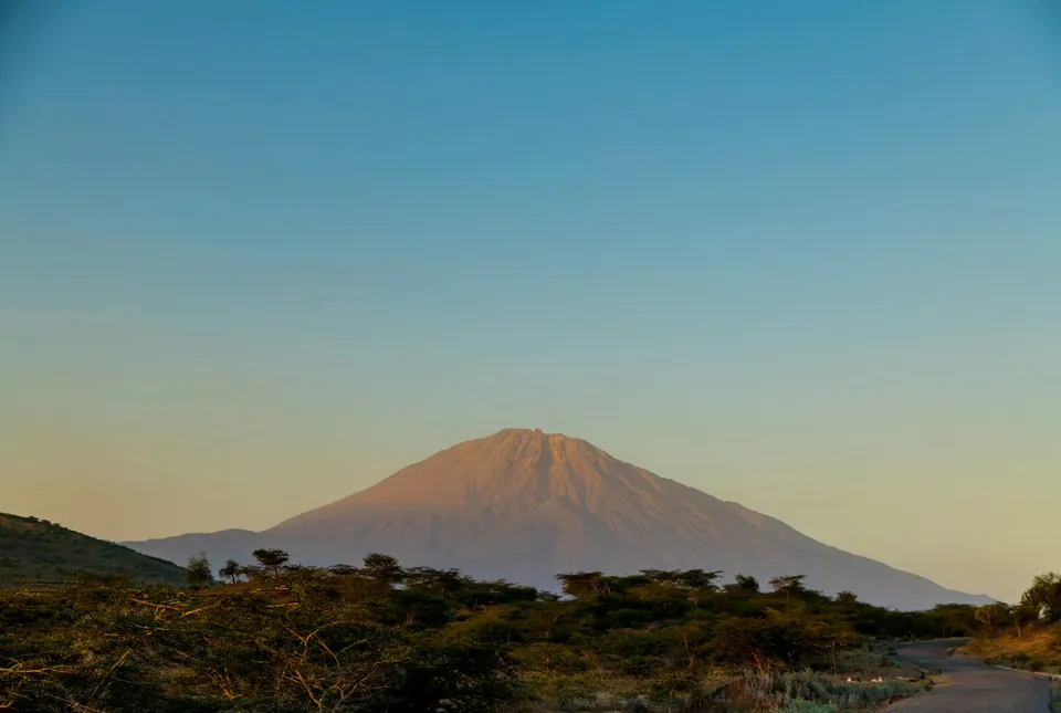 Mount Meru glowing at sunset above acacia bush and a quiet road